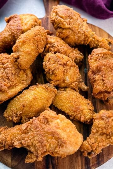 A wooden board topped with a spread of freshly fried, crispy chicken drumsticks, thighs, and wings, showcasing golden brown, crunchy coating.